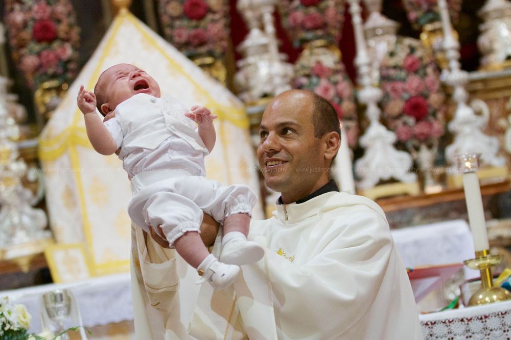 Religious ceremony with baby being held up in white garments against ornate backdrop.