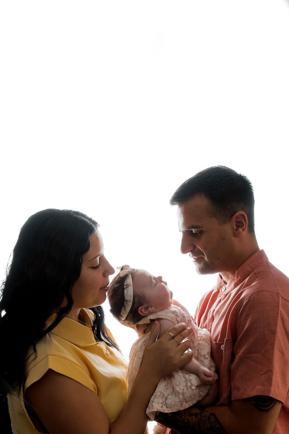 Parents lovingly holding their newborn baby together, sharing a tender family moment against a bright white background.