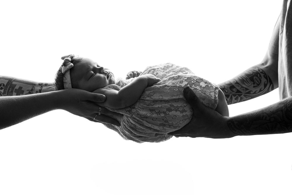 Black and white photo of parents cradling their newborn baby, a tender family moment captured in soft light.
