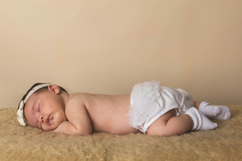 Newborn baby sleeping peacefully on a fluffy blanket, wearing white bloomers and a headband.