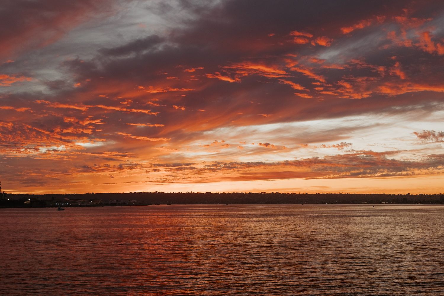 Dramatic orange and red sunset sky reflects off calm ocean waters creating a stunning panoramic seascape view in San Diego.