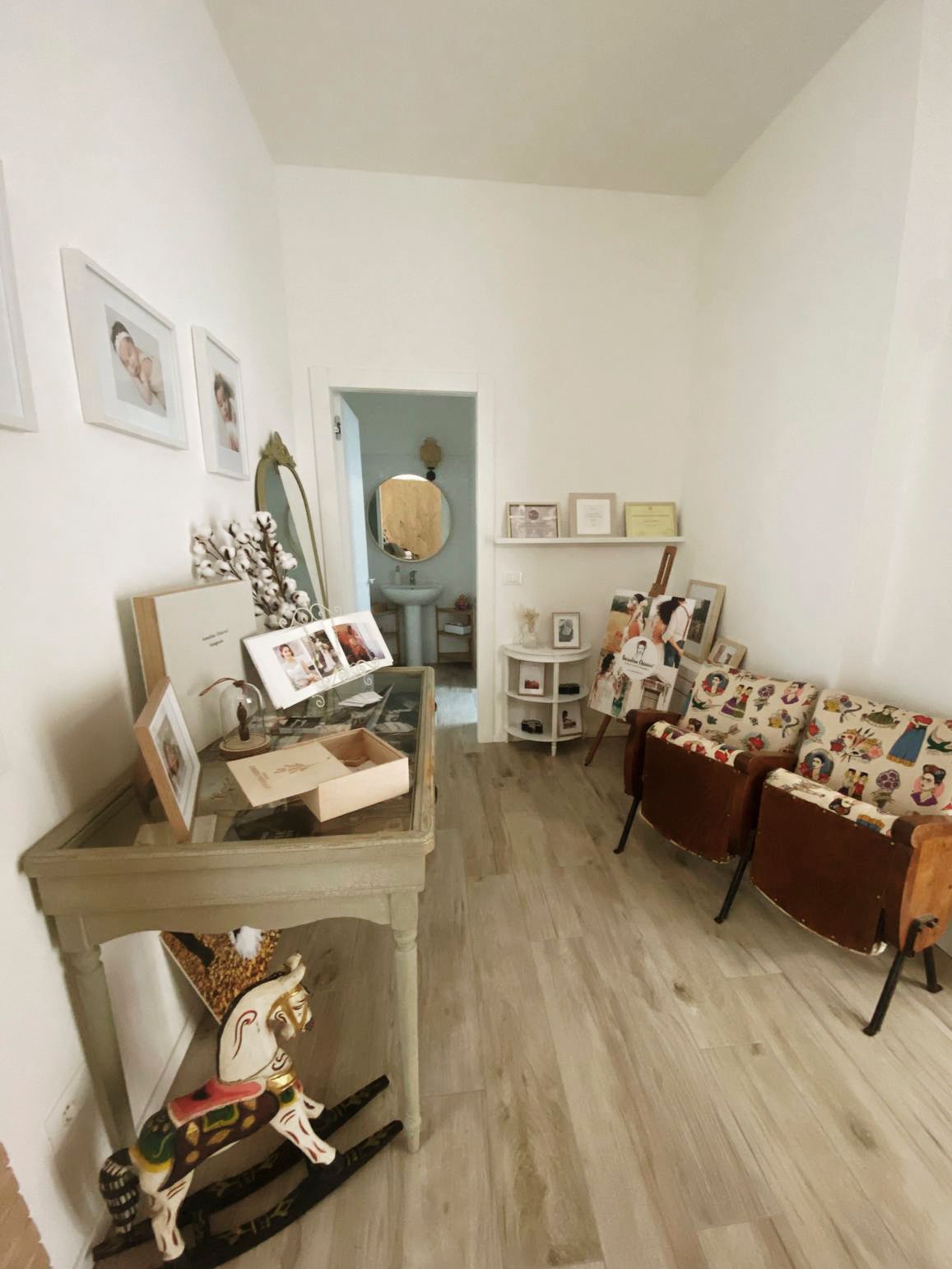 A vintage-styled photography studio space with a wooden rocking horse, display tables, and framed photographs on white walls.
