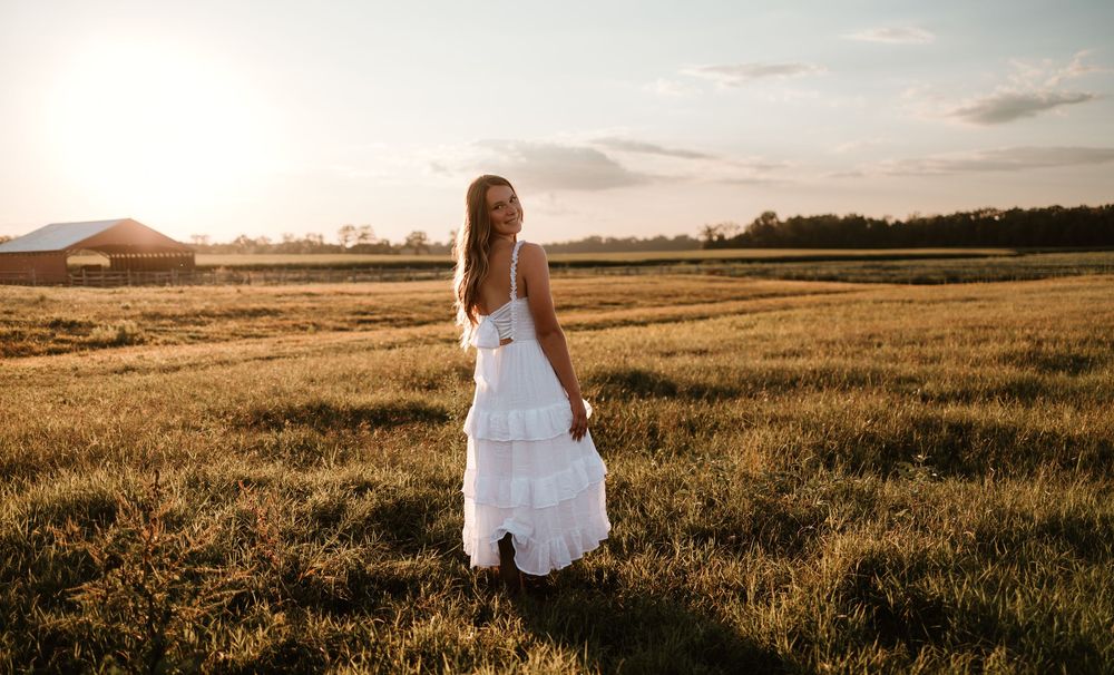 A white wedding dress flows gracefully across a golden wheat field at sunset creating a romantic silhouette.