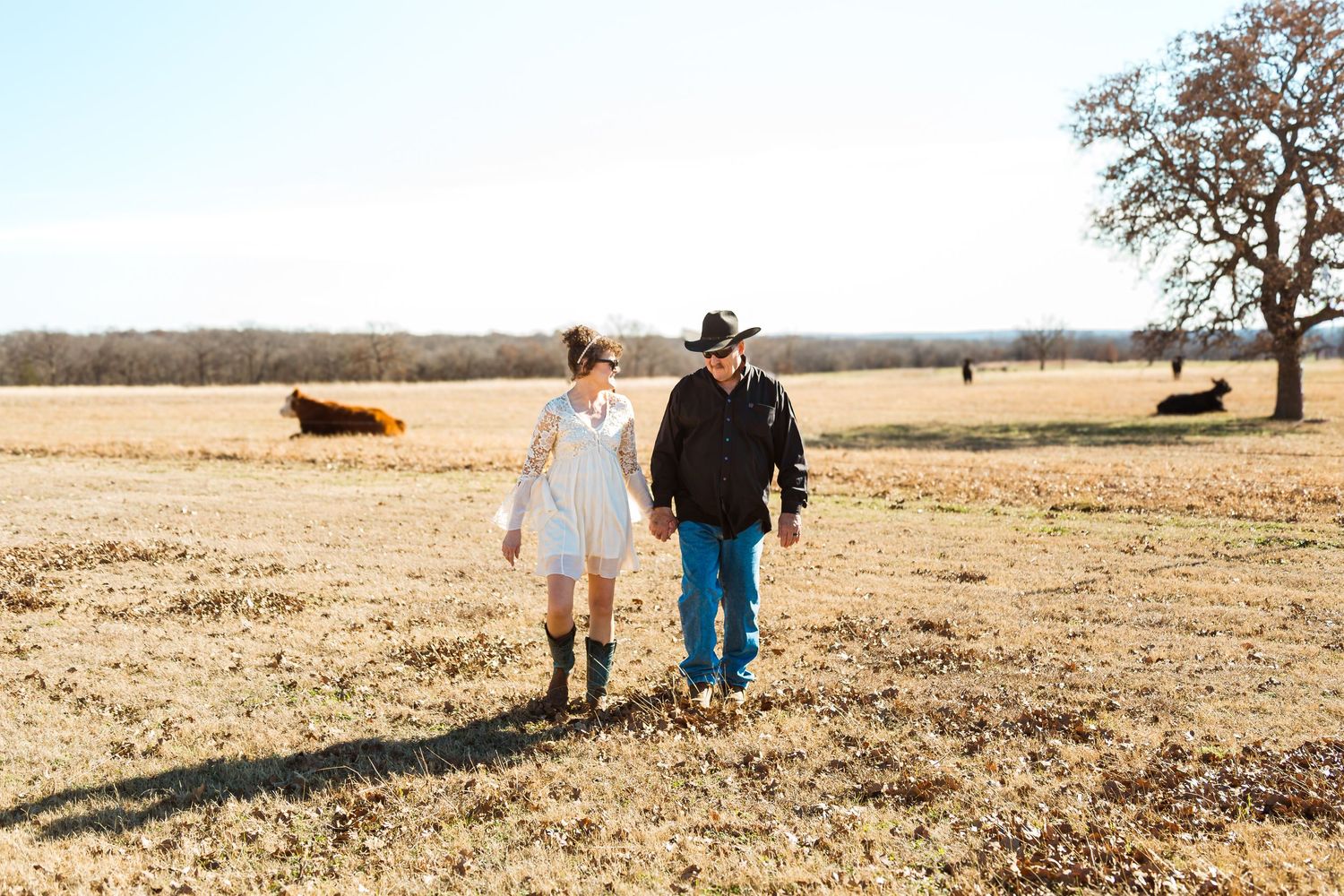 A couple walks through a golden field with their dogs during a sunny autumn day.