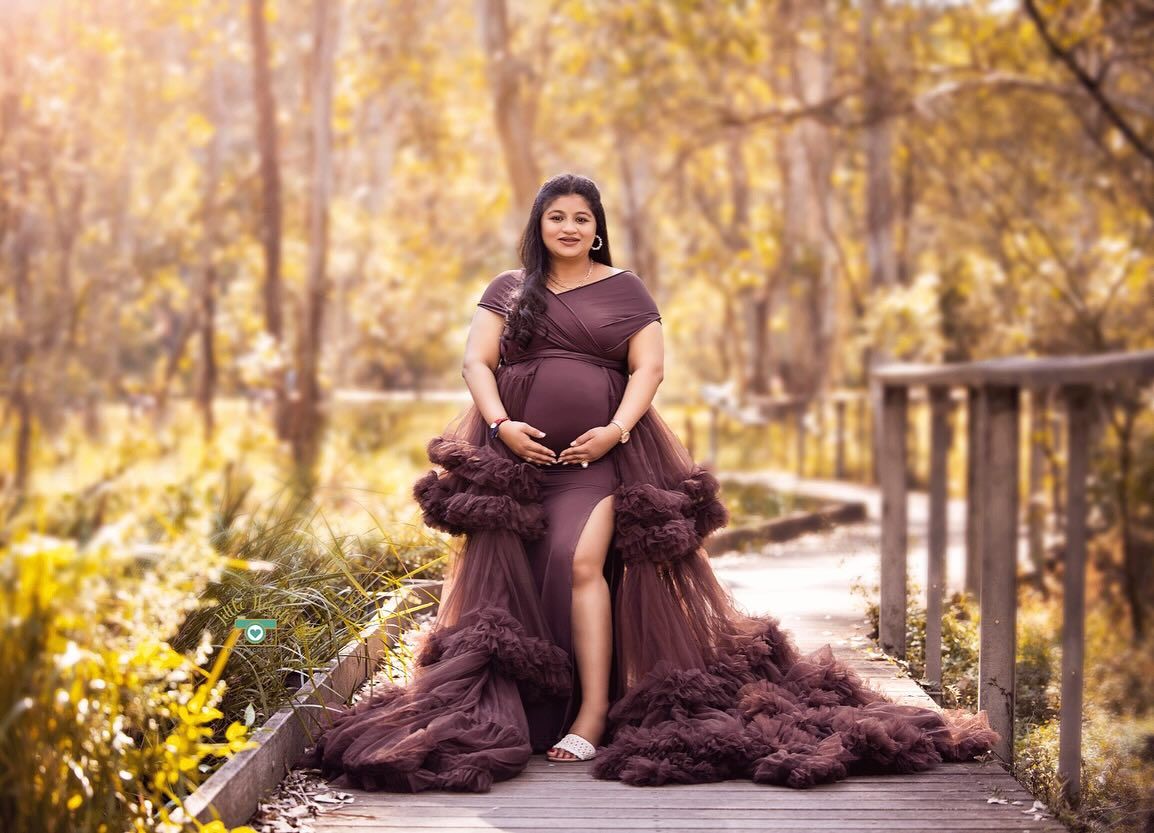 A maternity photo shoot in a purple dress on a wooden bridge during golden autumn sunset.