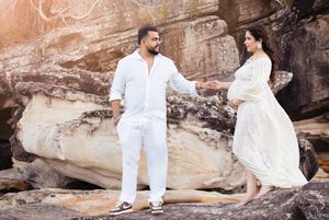 Two people in white outfits pose on rocky cliffs during a romantic photo session at sunset.