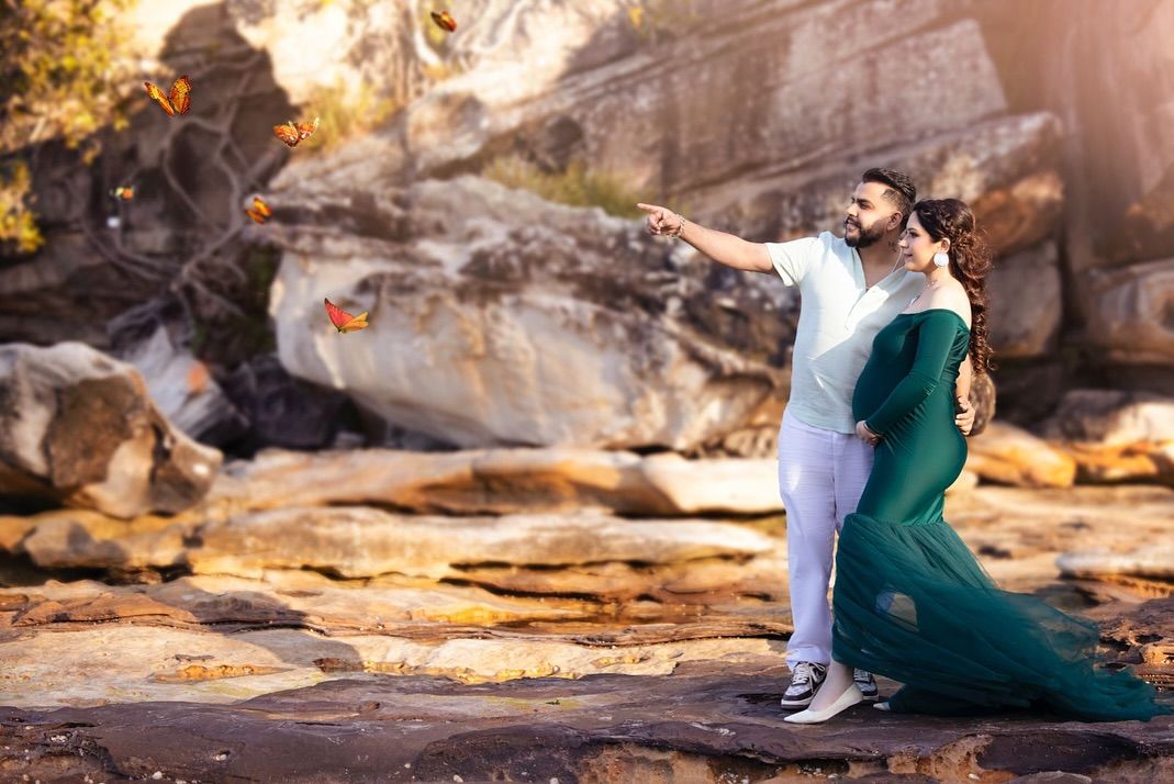 A couple in green and white outfits sits together on rocky terrain during golden hour lighting.