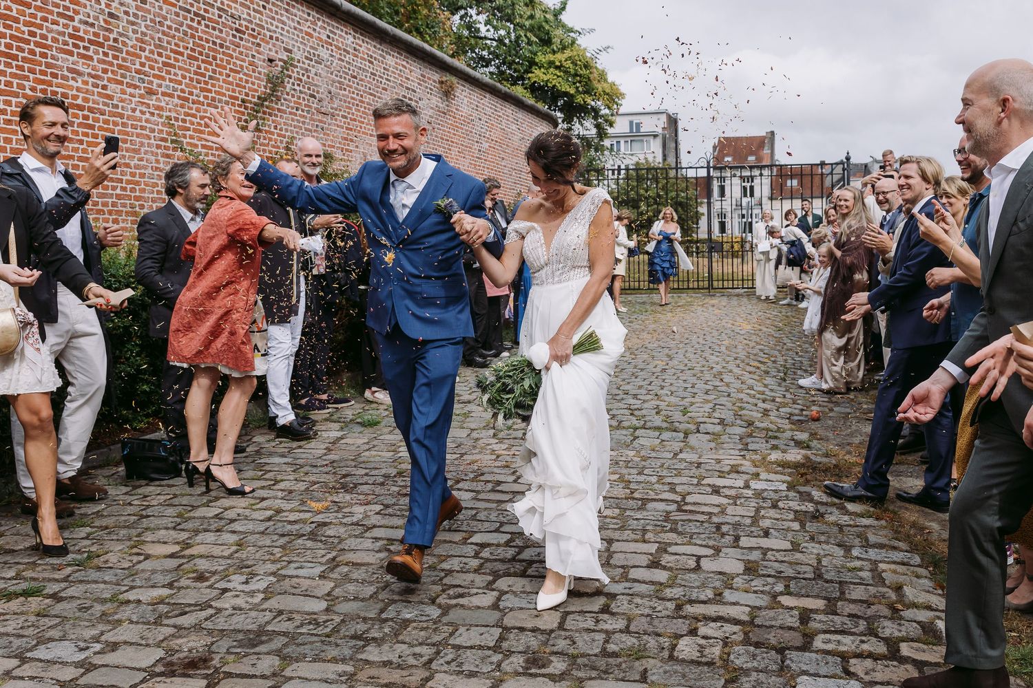 Wedding guests celebrate and dance together on a cobblestone street outside a historic brick building.