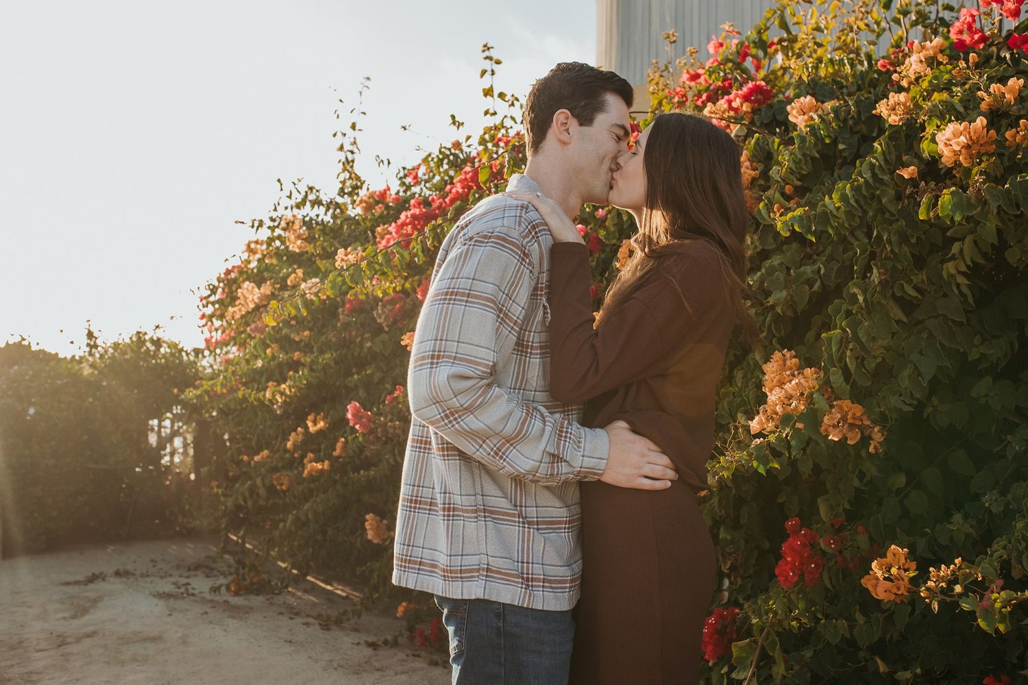 A couple embraces in front of a vibrant orange bougainvillea bush during golden hour sunset at Windansea Beach in La Jolla.