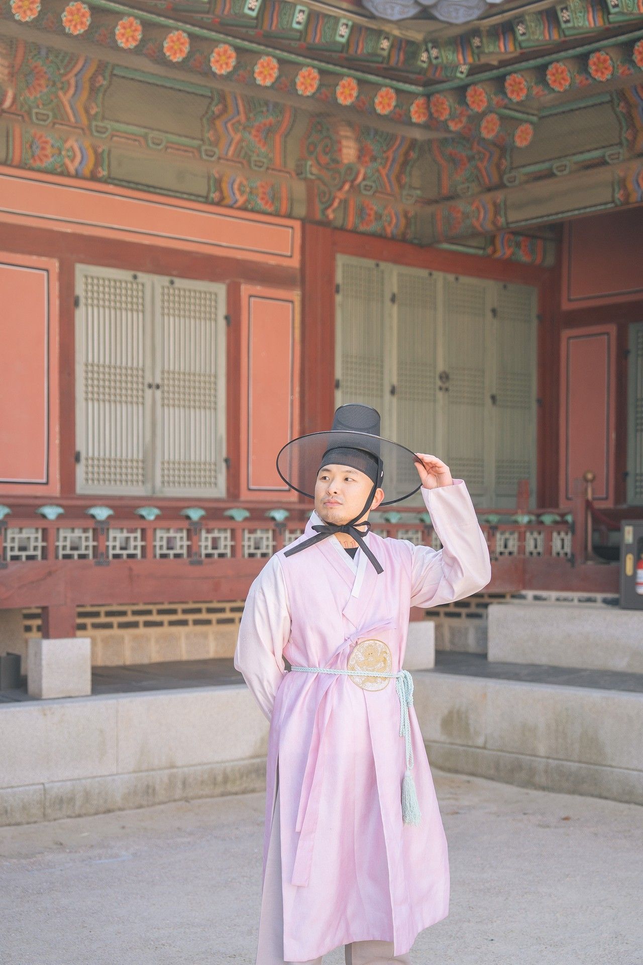Traditional Korean palace guard in pink hanbok and black hat performs ceremonial gestures at Gyeongbokgung Palace.
