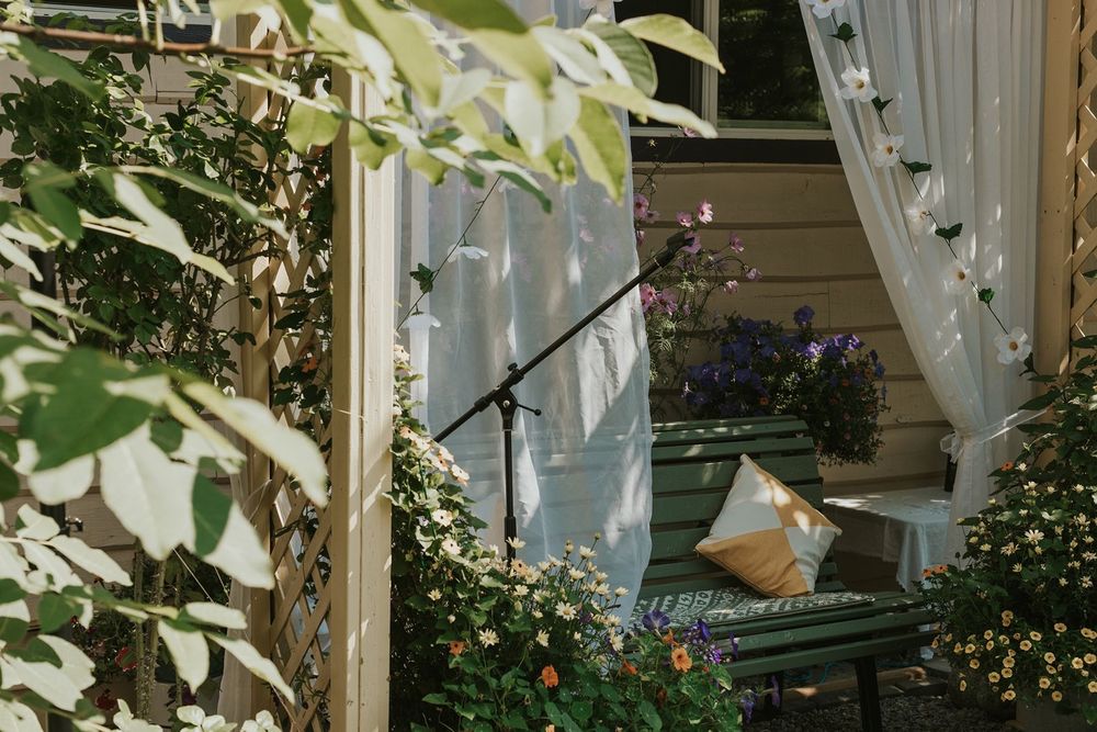 Charming garden wedding arbor decorated with flowers, white curtains, and a cushioned bench.