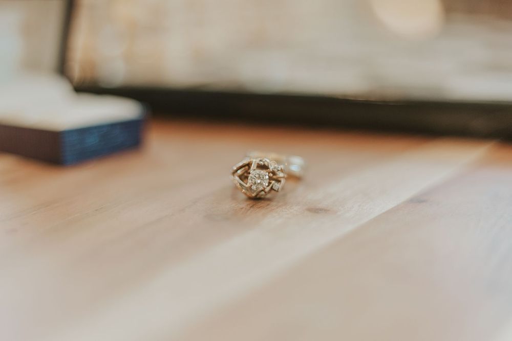Close-up of an elegant diamond engagement ring resting on a wooden surface near a ring box.