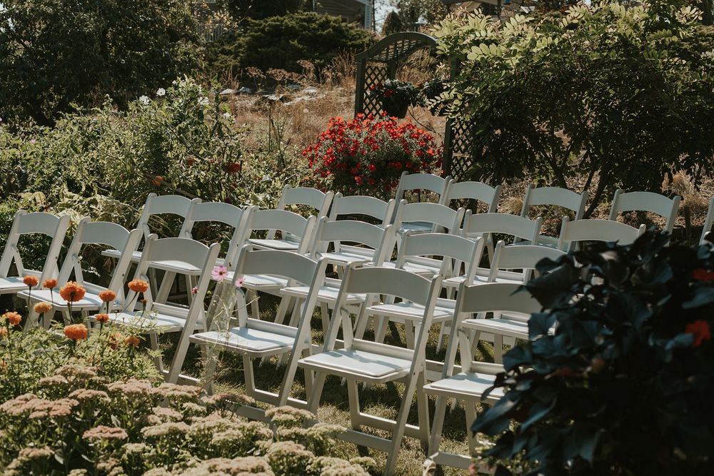 Rows of white folding chairs set up outdoors in a garden for a wedding ceremony.