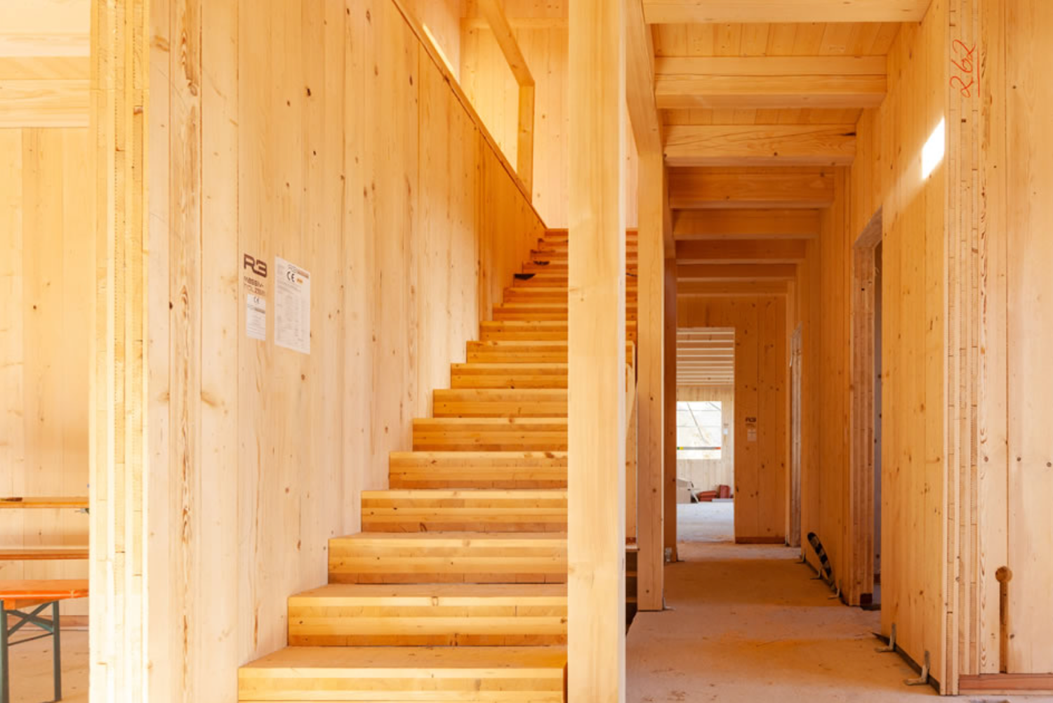 Long wooden corridor with natural light illuminating the path and stairs leading upward in a modern building interior.