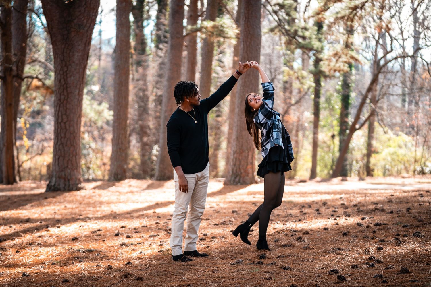 People hiking through a scenic autumn forest trail with tall trees and fallen leaves on the ground.