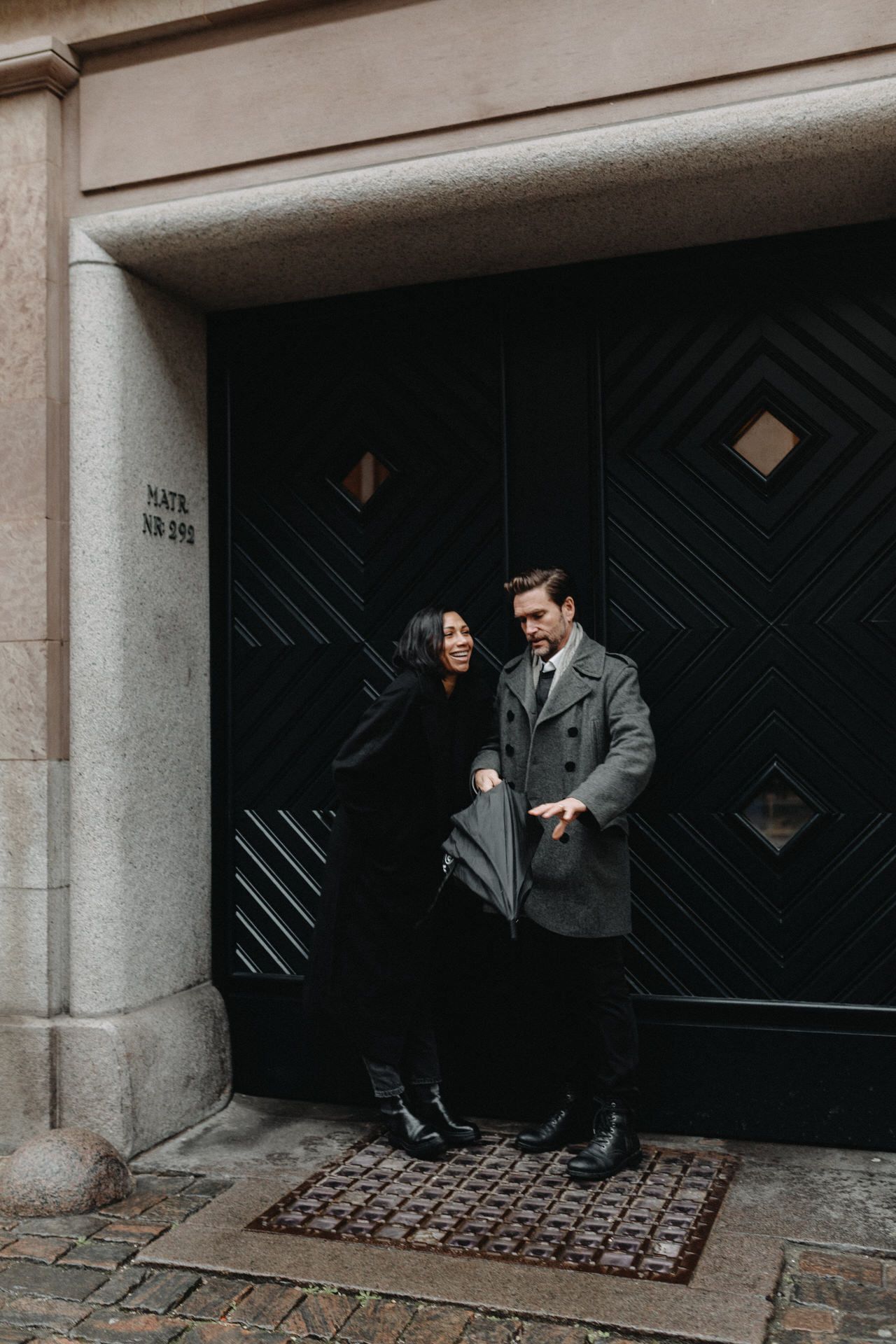 A couple stands near a decorative doorway with geometric patterns in a dimly lit architectural space.
