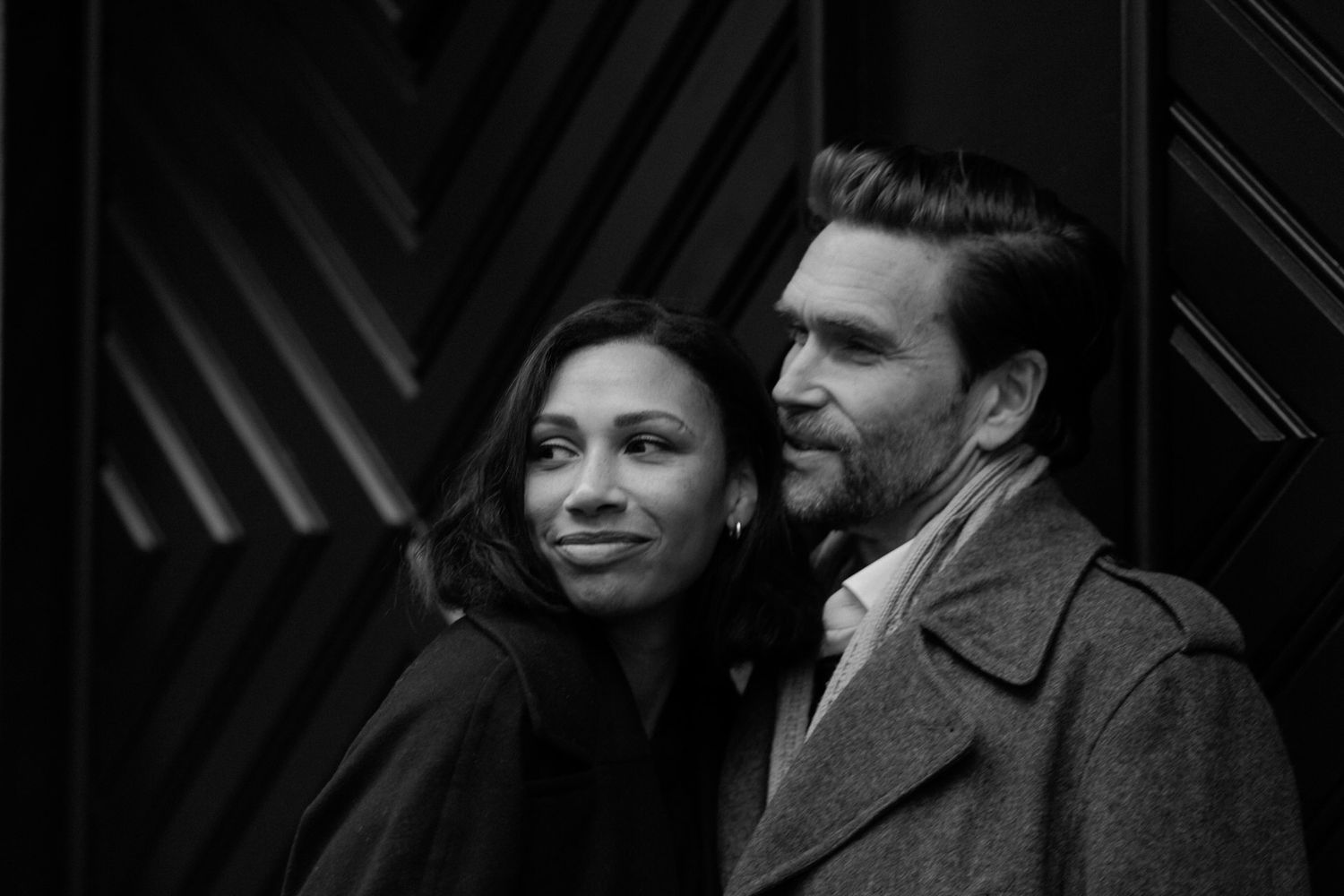 A black and white photograph shows people standing in a dark interior space with dramatic lighting.
