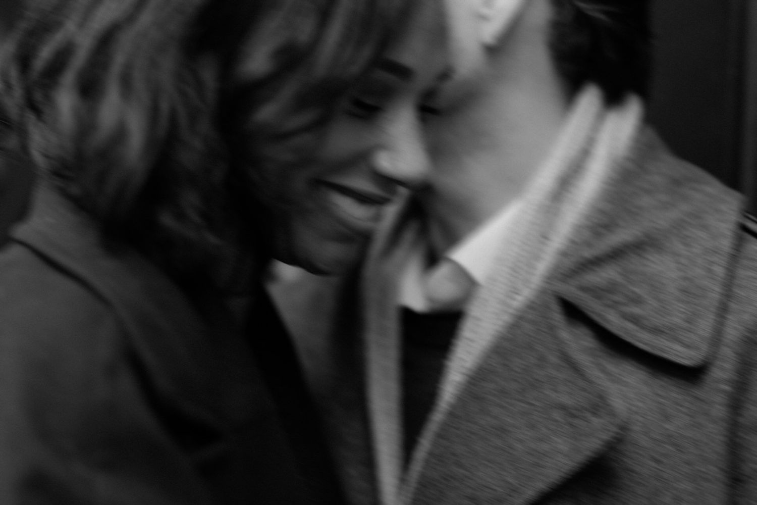 A blurred black and white intimate moment between a couple in winter coats.