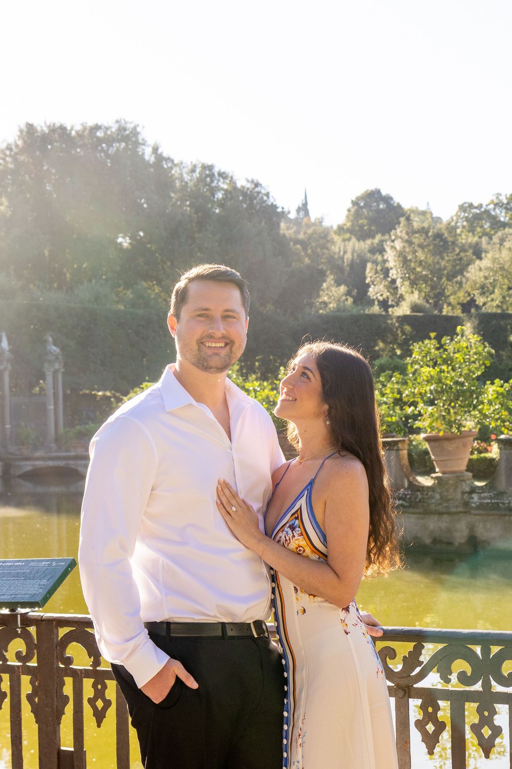 Couple shares romantic moments at sunset by a decorative railing overlooking water.
