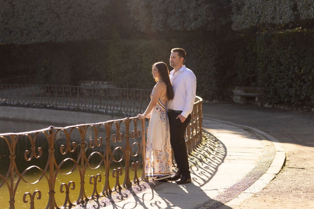 A couple shares a romantic moment at sunset while standing against an ornate iron railing.