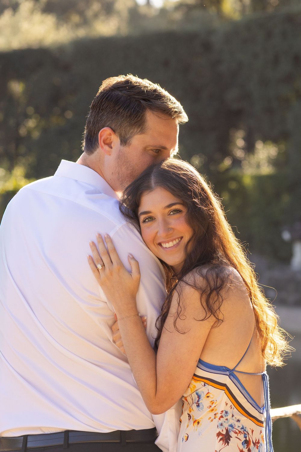 Couple embraces in warm sunlight during outdoor photo session by ornate railing.