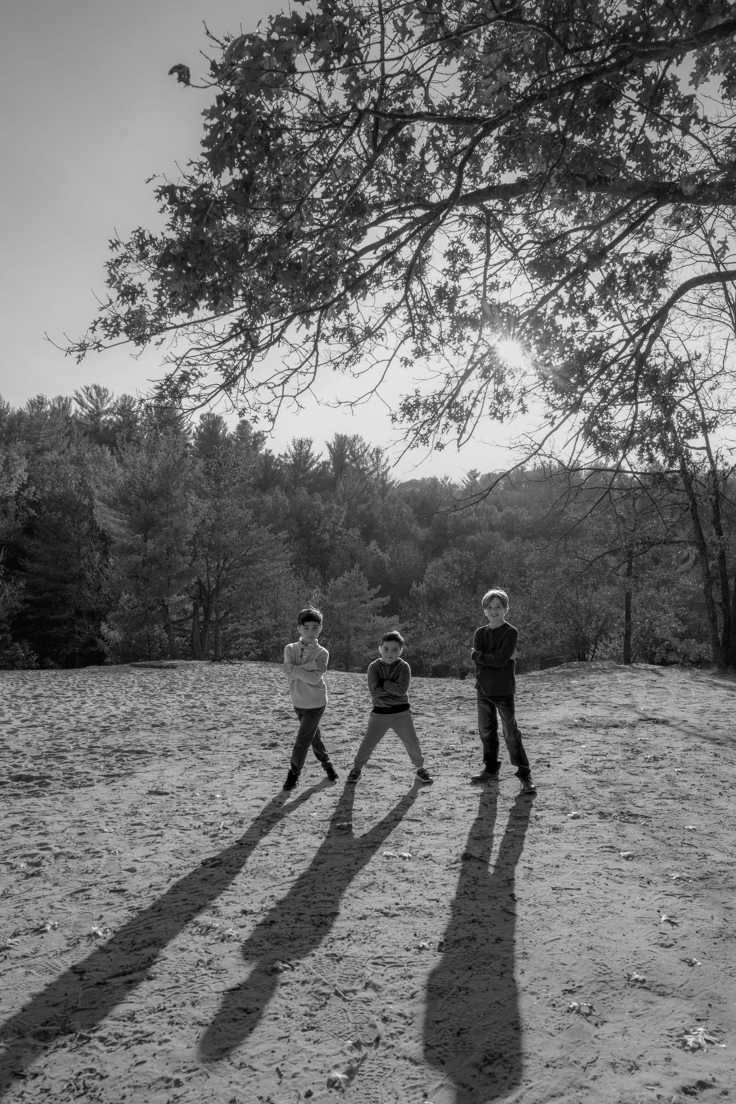 Three people cast long dramatic shadows while standing on a snowy hill in black and white photography.
