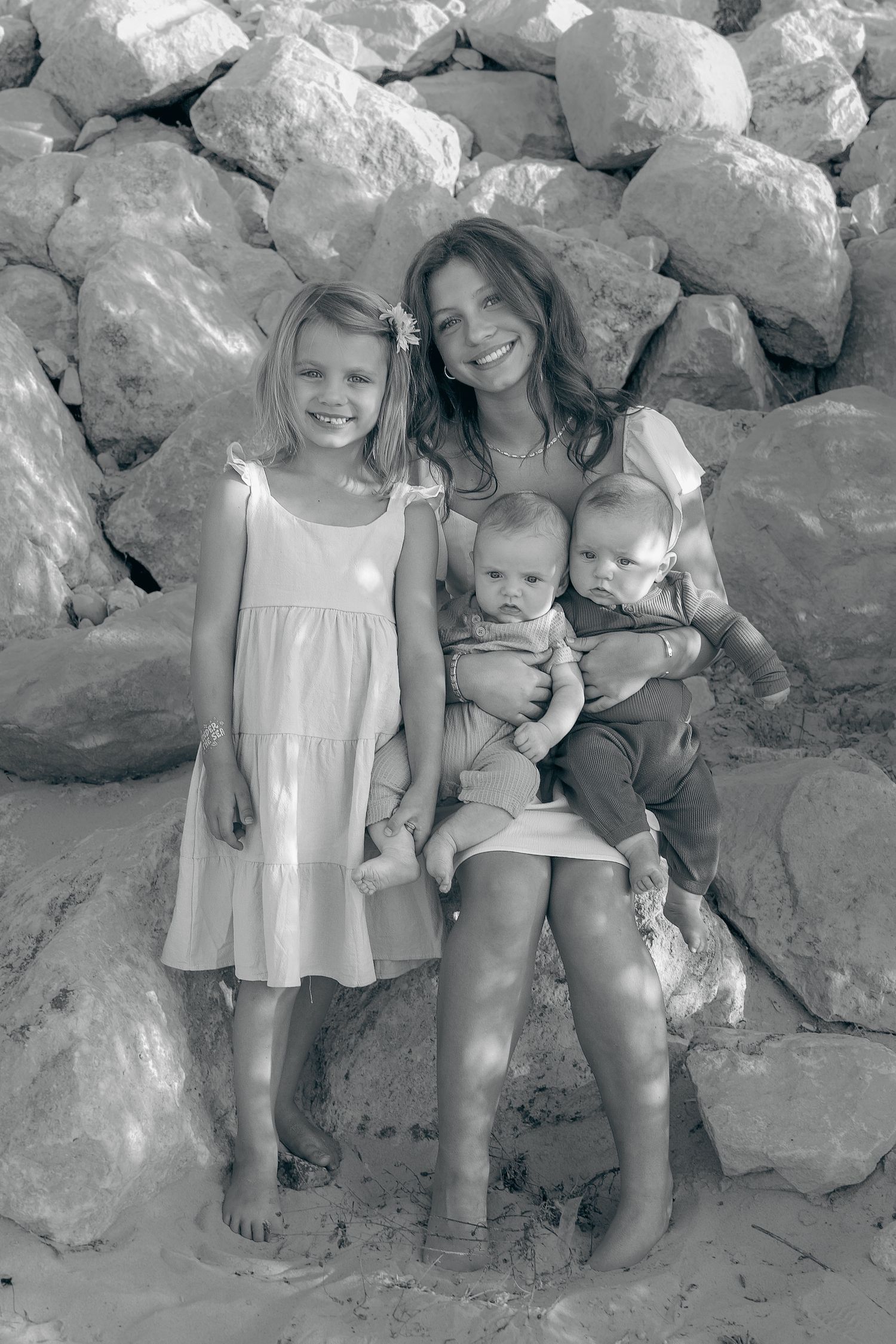 Black and white portrait of a family sitting together on rocky beach terrain.