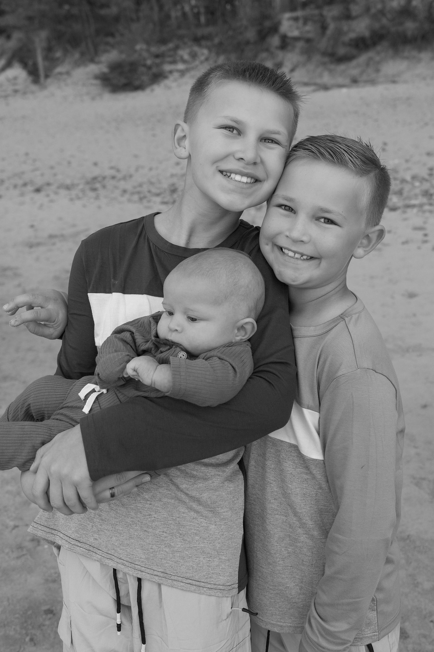 Black and white portrait of three siblings sharing a joyful moment together outdoors.