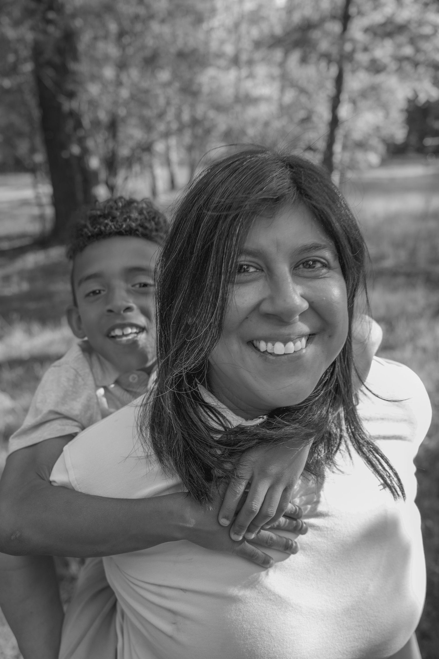 A black and white portrait of a parent and child sharing a joyful moment outdoors.