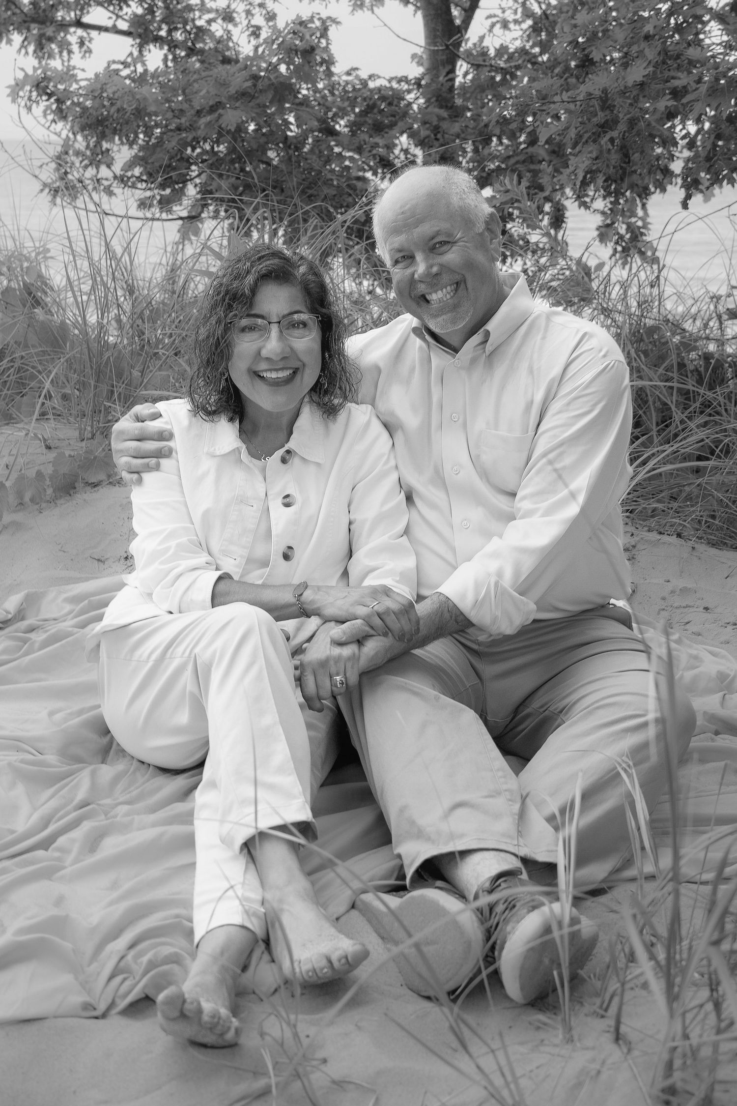 A couple sitting together outdoors in white clothing sharing joyful moments in a black and white photo series.