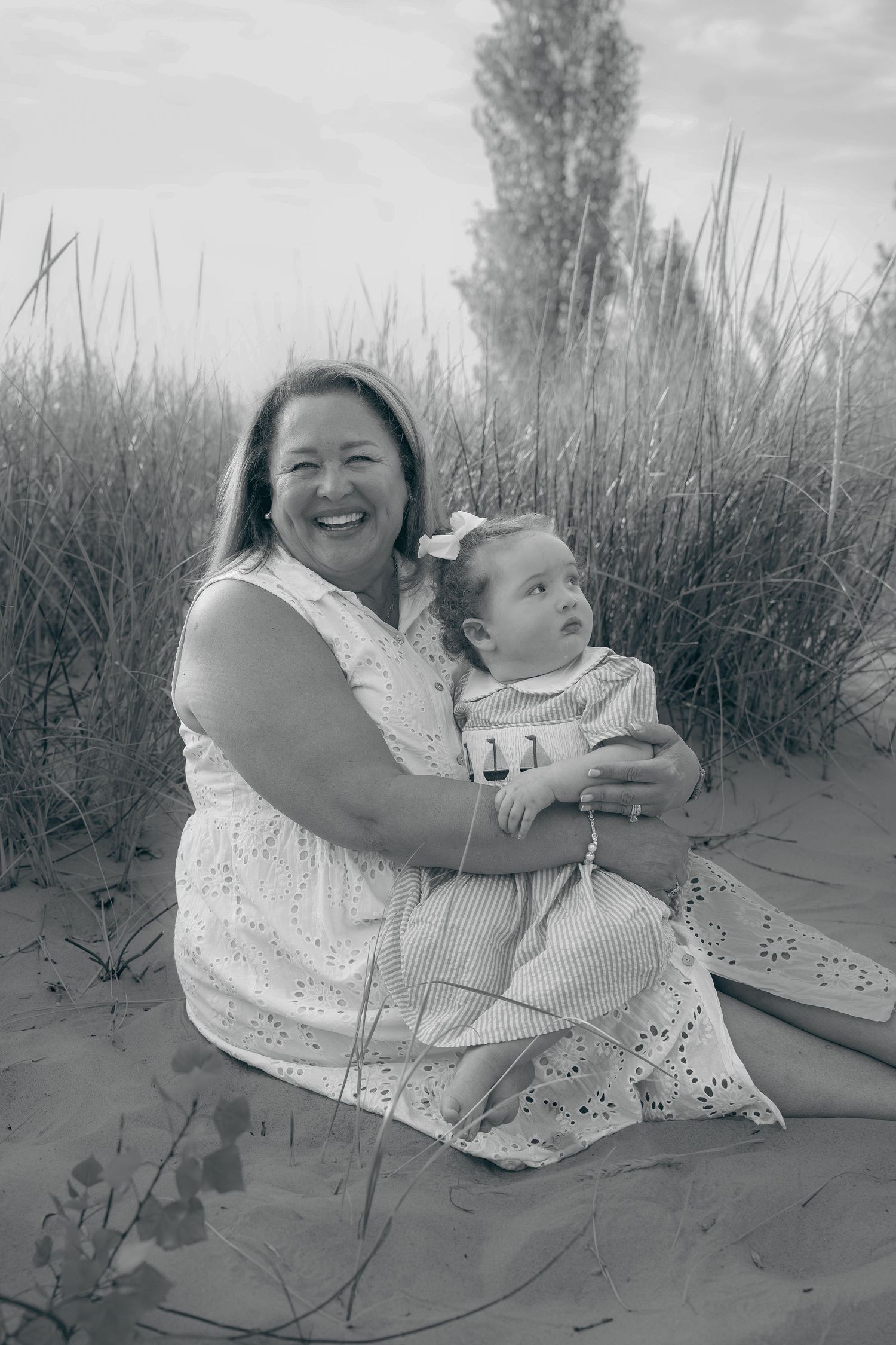 Black and white photo series of two people sharing joyful moments together on a sandy beach with tall grass.