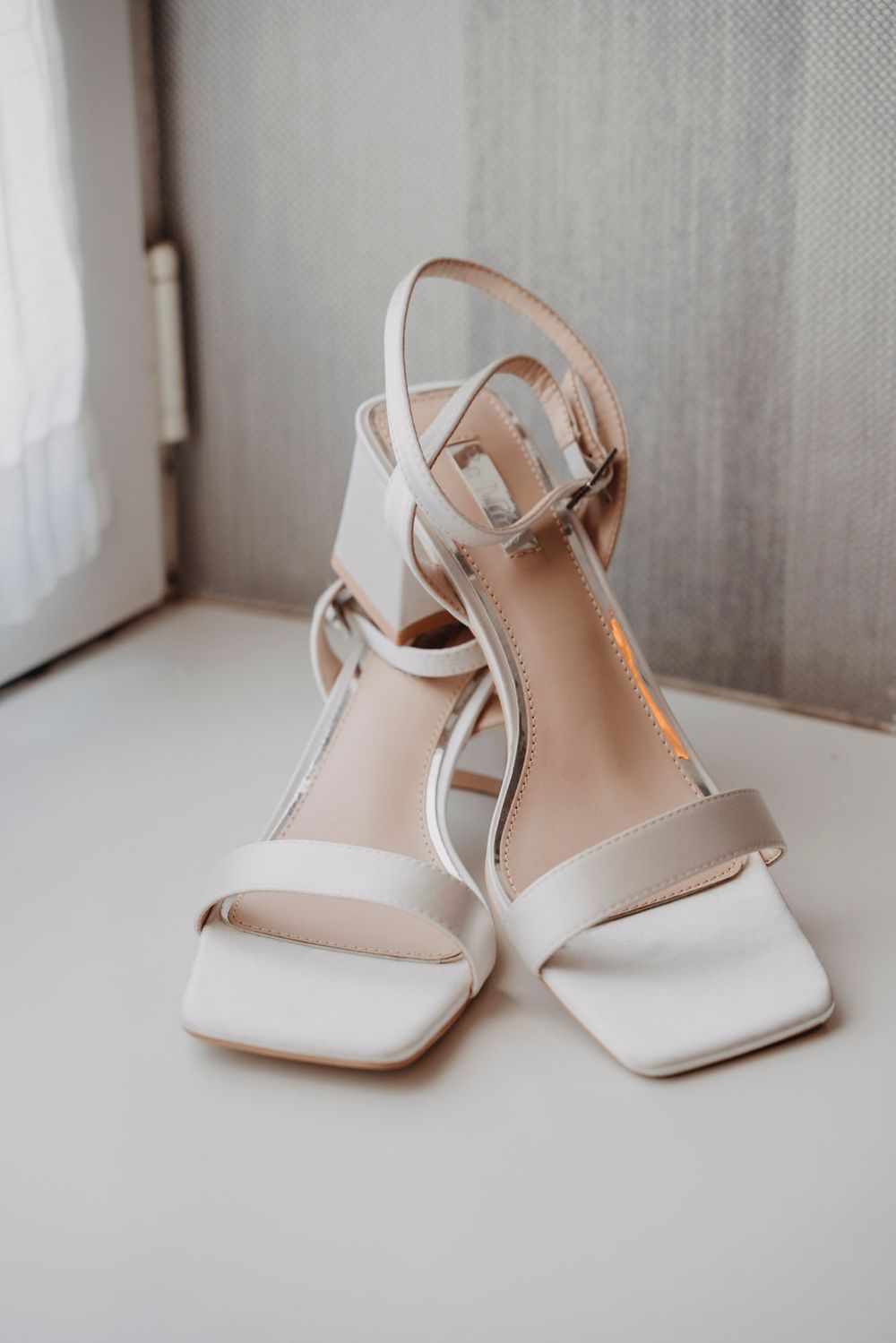 Elegant white bridal heels displayed against a neutral background.