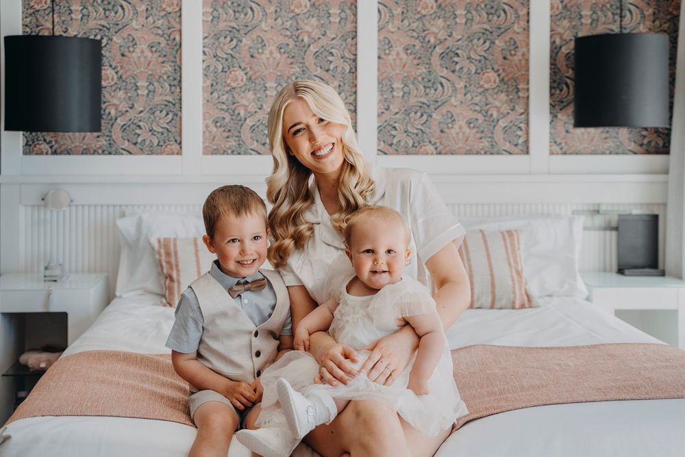 Family relaxing together on bed with soft pink and gray decor.