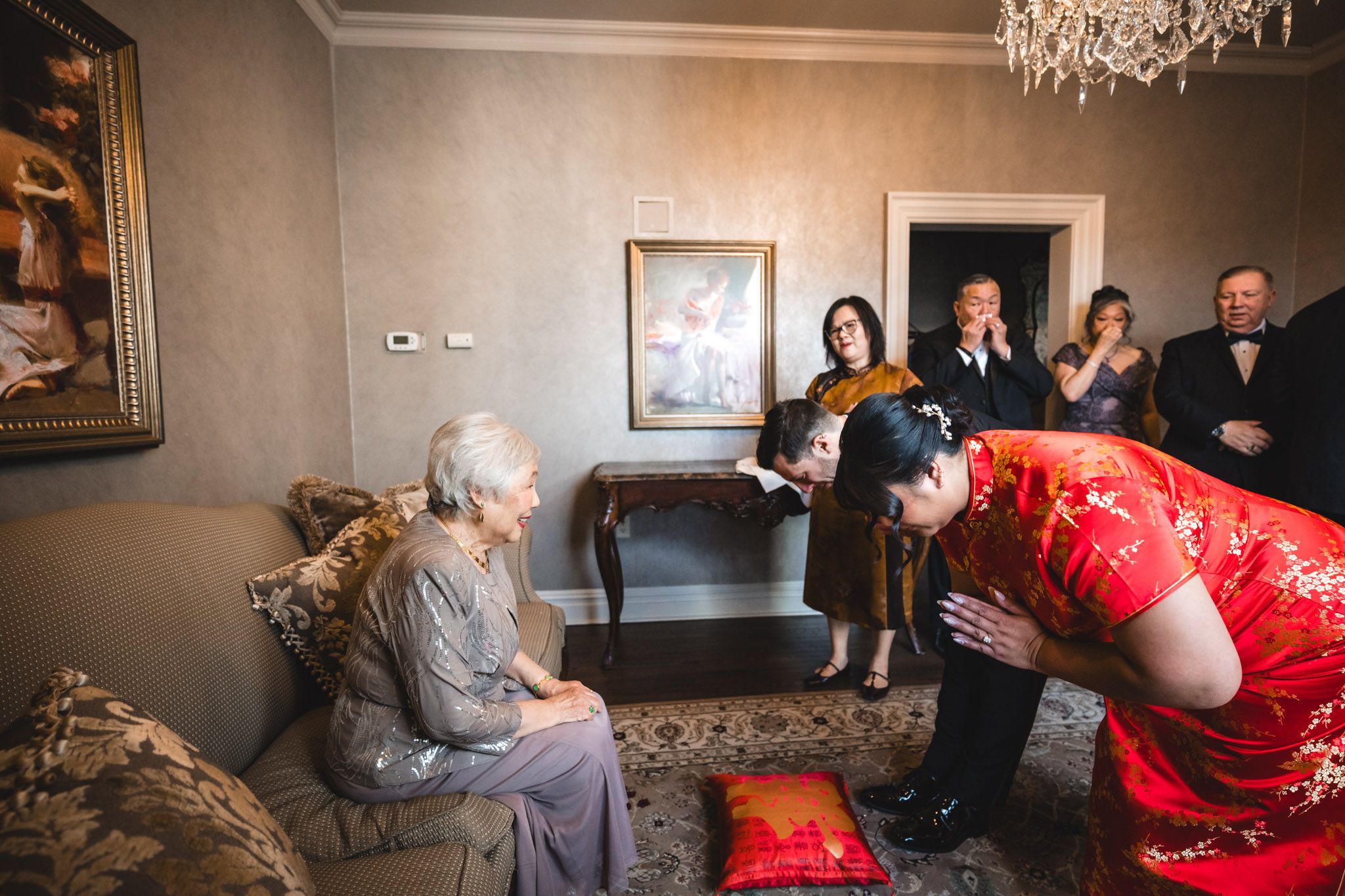 Traditional tea ceremony with guests in formal attire gathered in elegant living room.