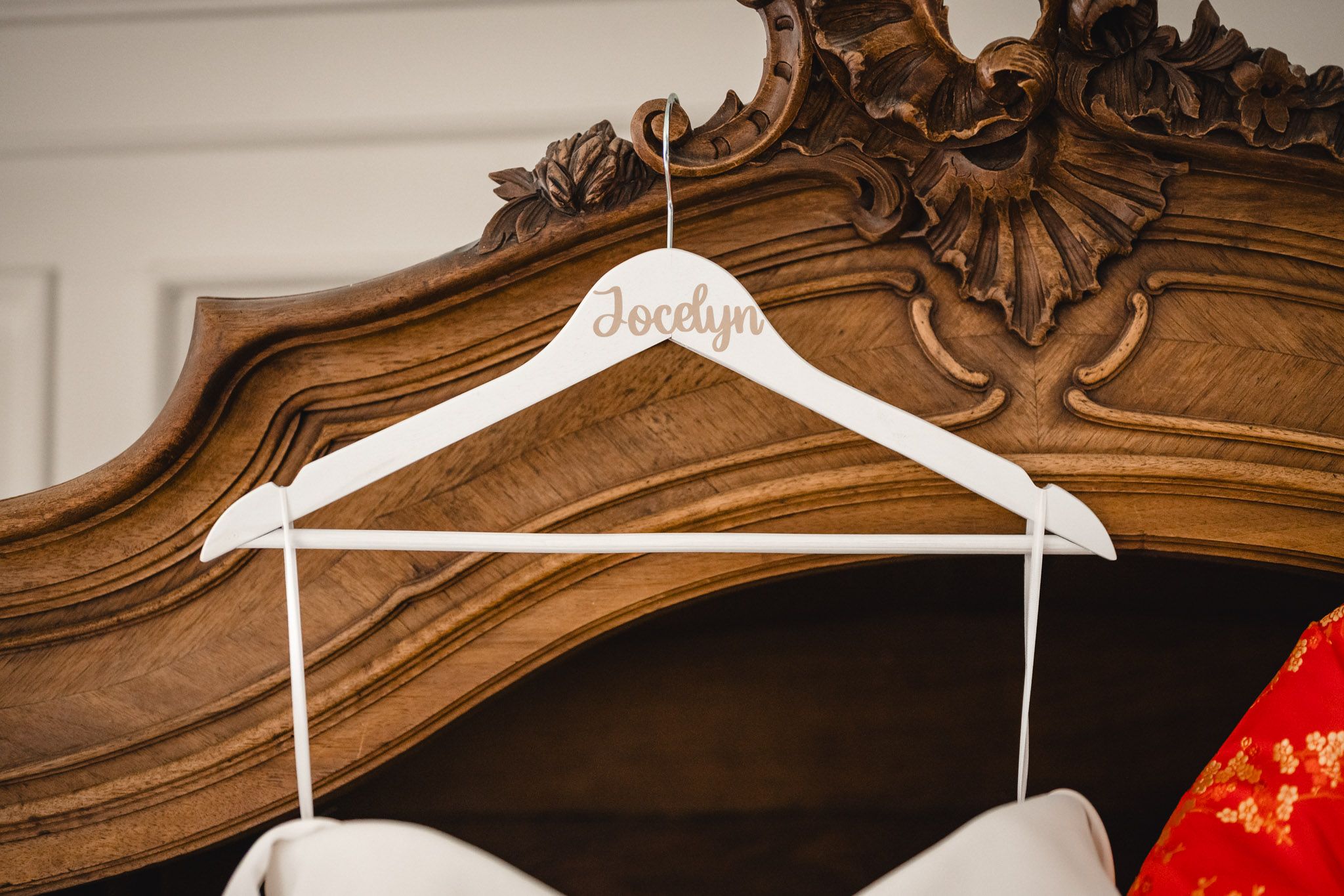 White wedding dress hanging on ornate wooden headboard with traditional Chinese dress beside it.