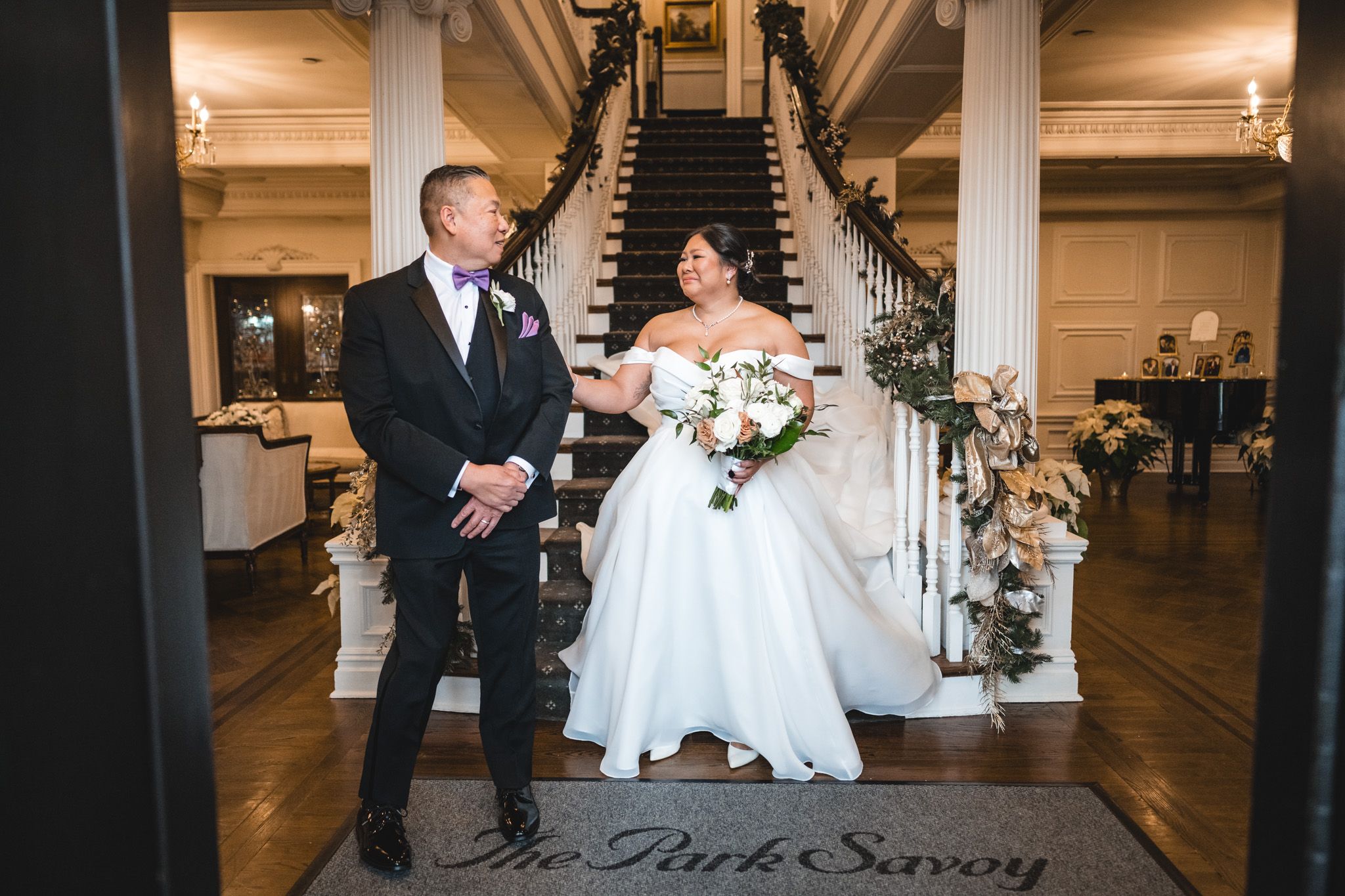 An elegant wedding portrait at the base of a grand staircase with decorative holiday touches.