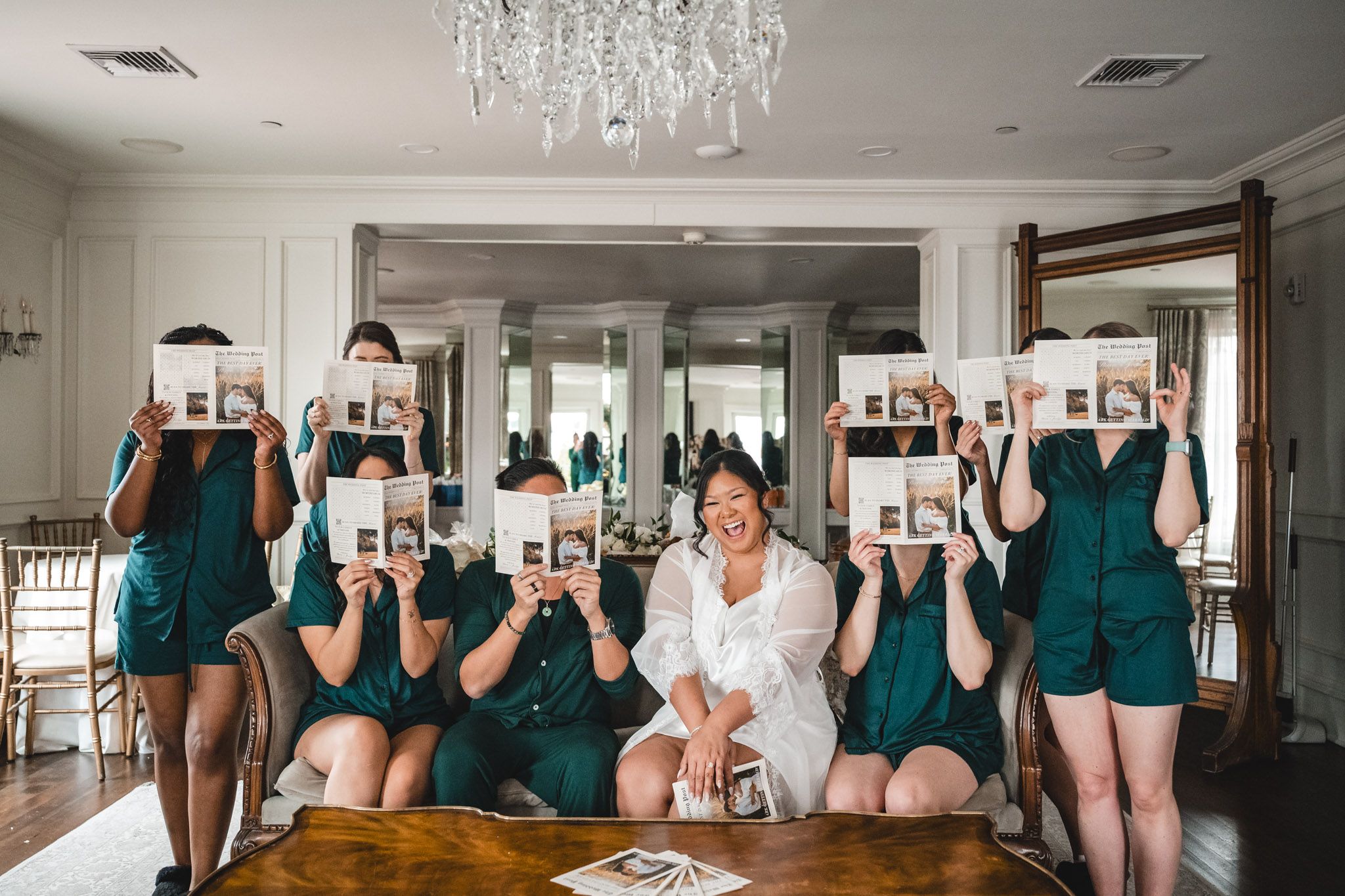 Wedding party in coordinated teal dresses posed in elegant room with chandelier.