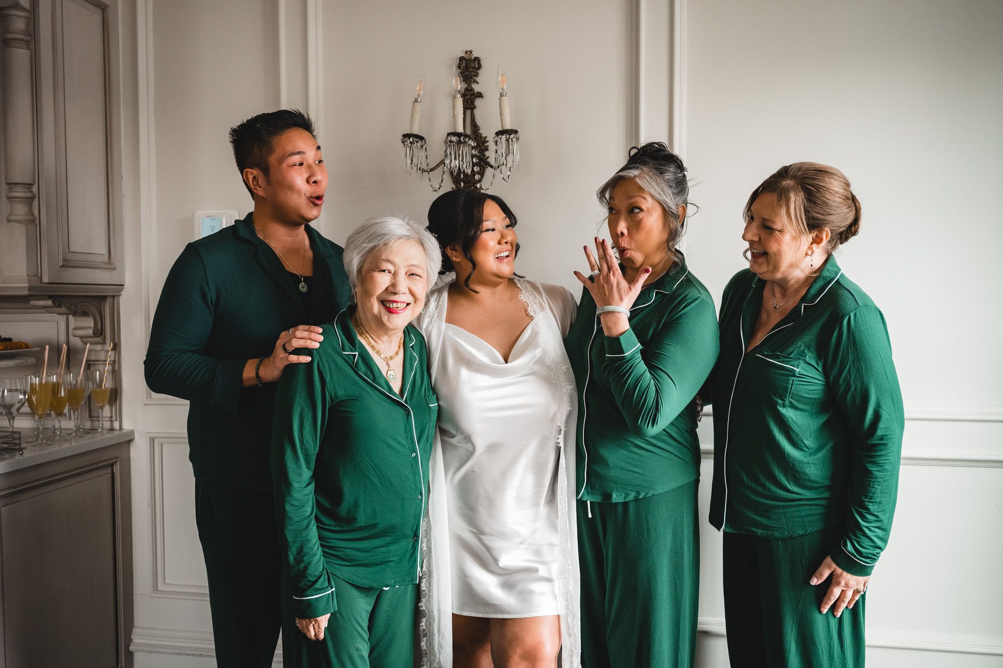Wedding party in emerald green dresses sharing joyful laughter in an elegant indoor setting.