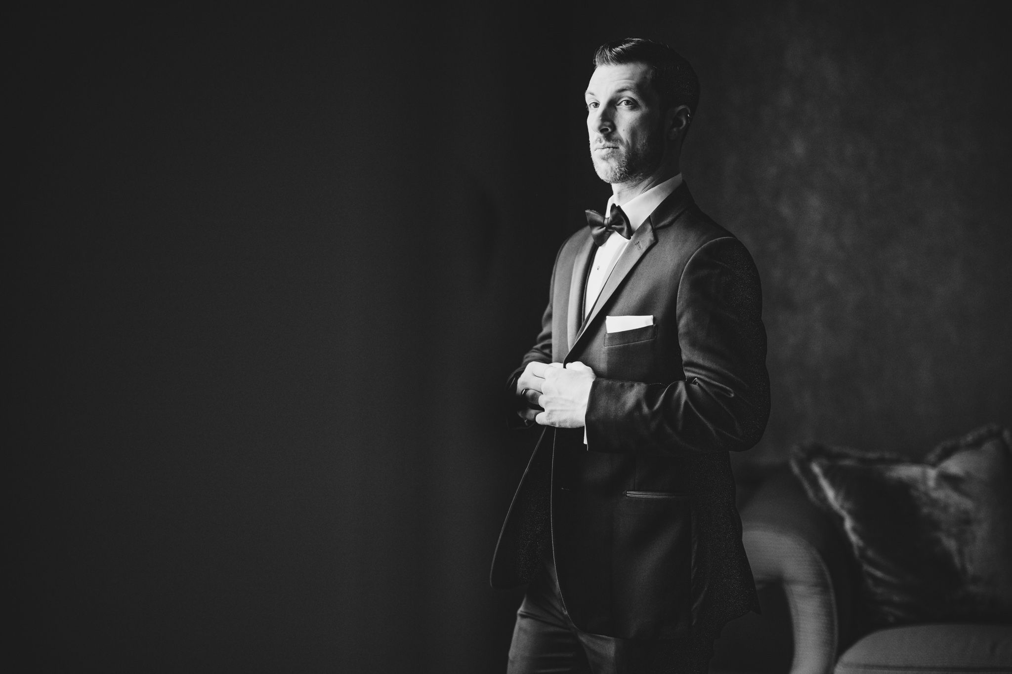 Dramatic black and white portrait of someone adjusting their tuxedo.