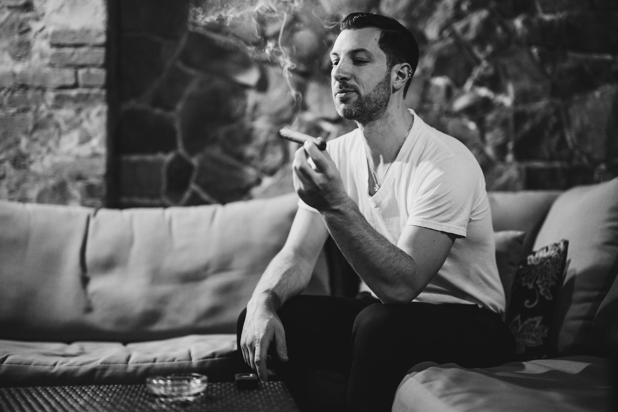 Black and white portrait of someone lighting a cigarette while seated on a couch.
