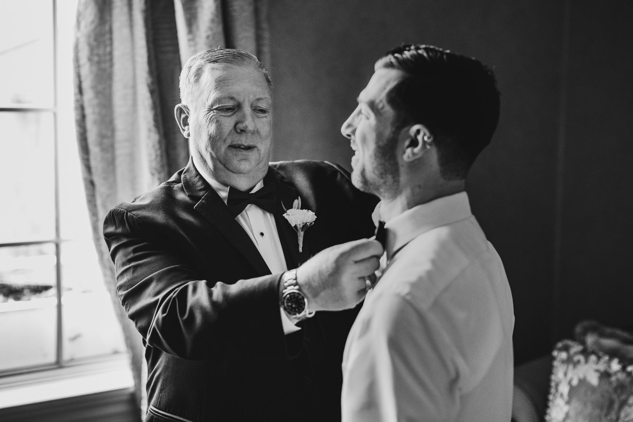 Black and white photo of formal attire preparation with bow tie adjustment.