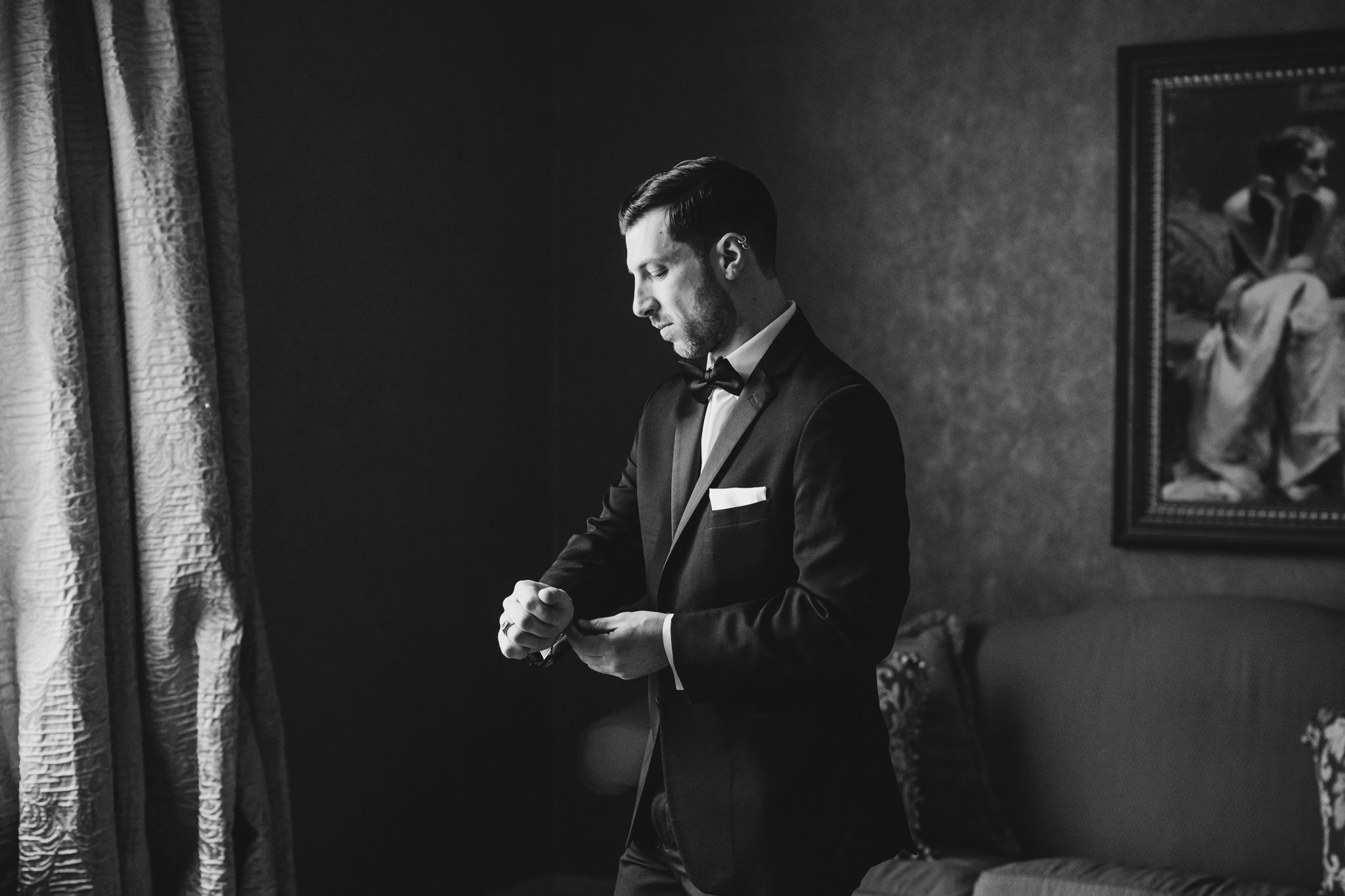 Black and white photo of someone adjusting their tuxedo cuffs in dim lighting.