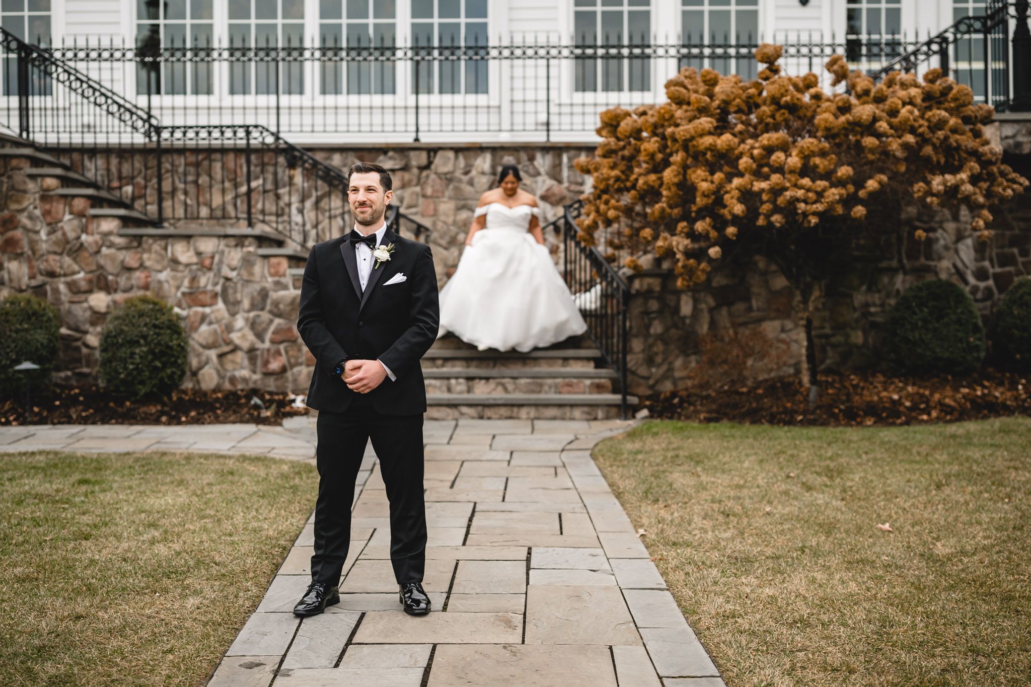 A wedding couple poses on a stone pathway with autumn foliage and a grand building in the background.