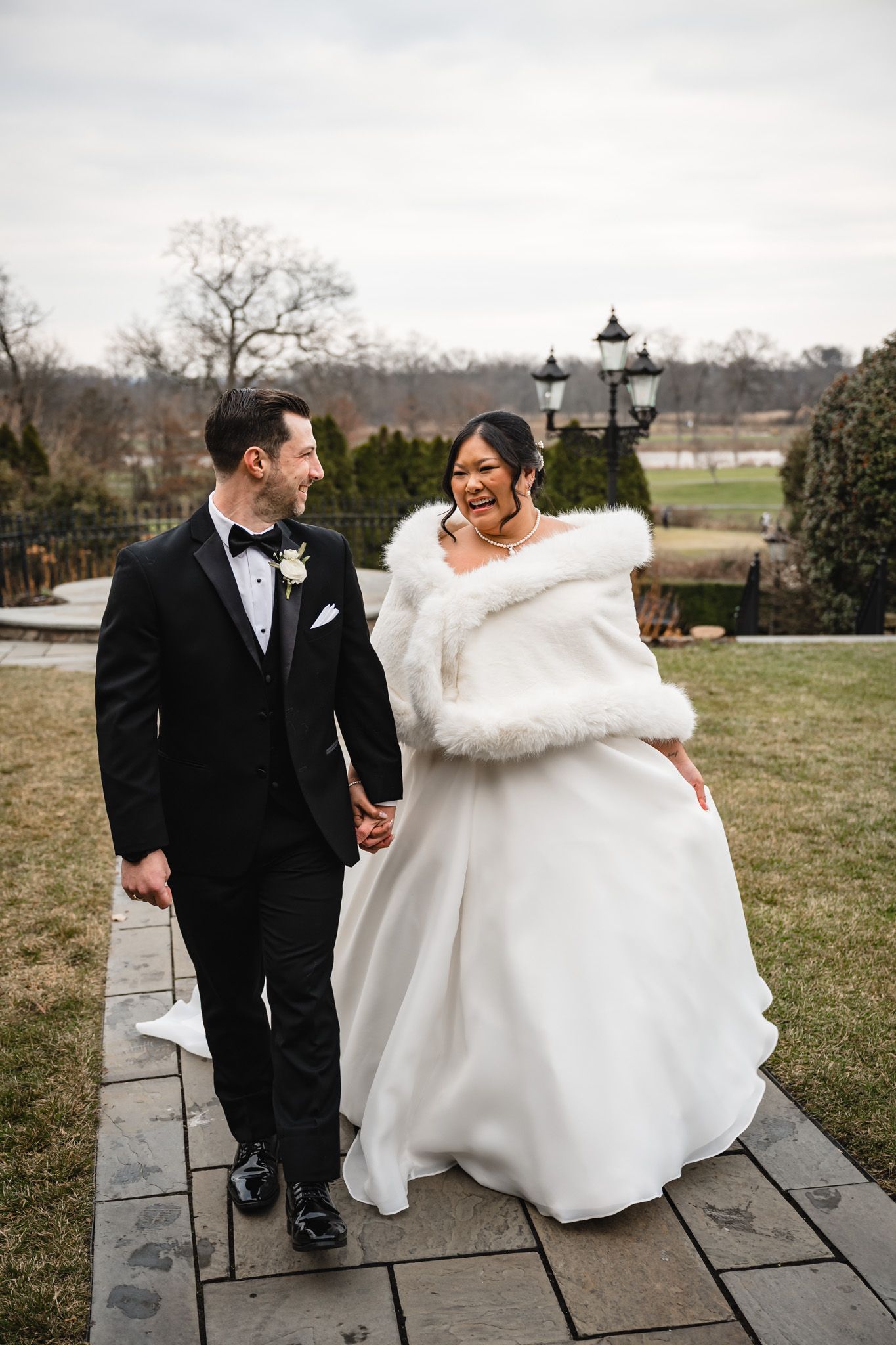 A winter wedding couple walks along a stone path wearing elegant attire with scenic views behind them.