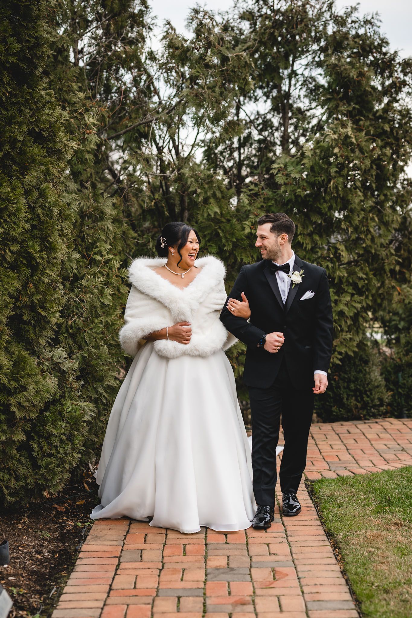 Wedding couple walks together on a brick path surrounded by greenery.