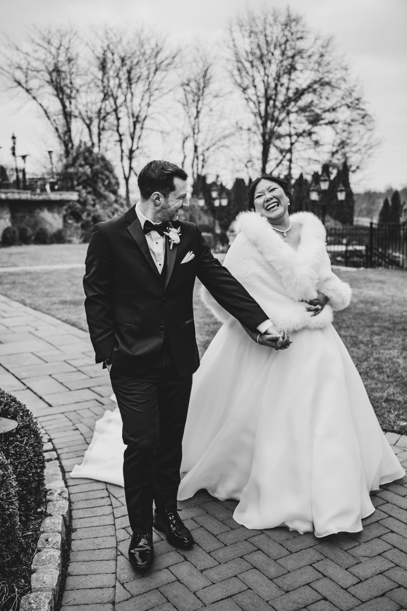 Black and white wedding photo of couple sharing a joyful moment on brick pathway.
