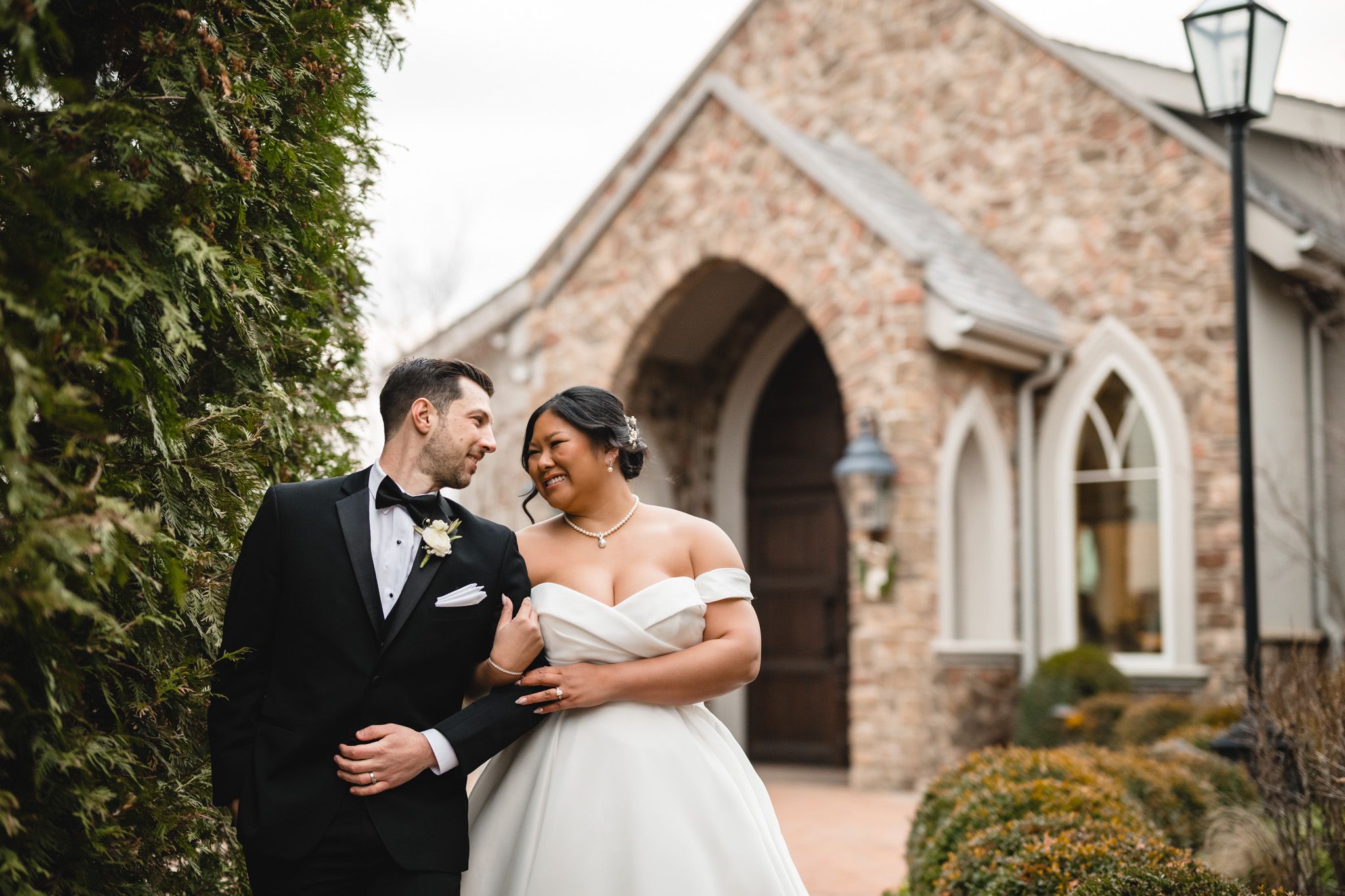 Candid wedding moment captured outside stone chapel with couple sharing laughter.