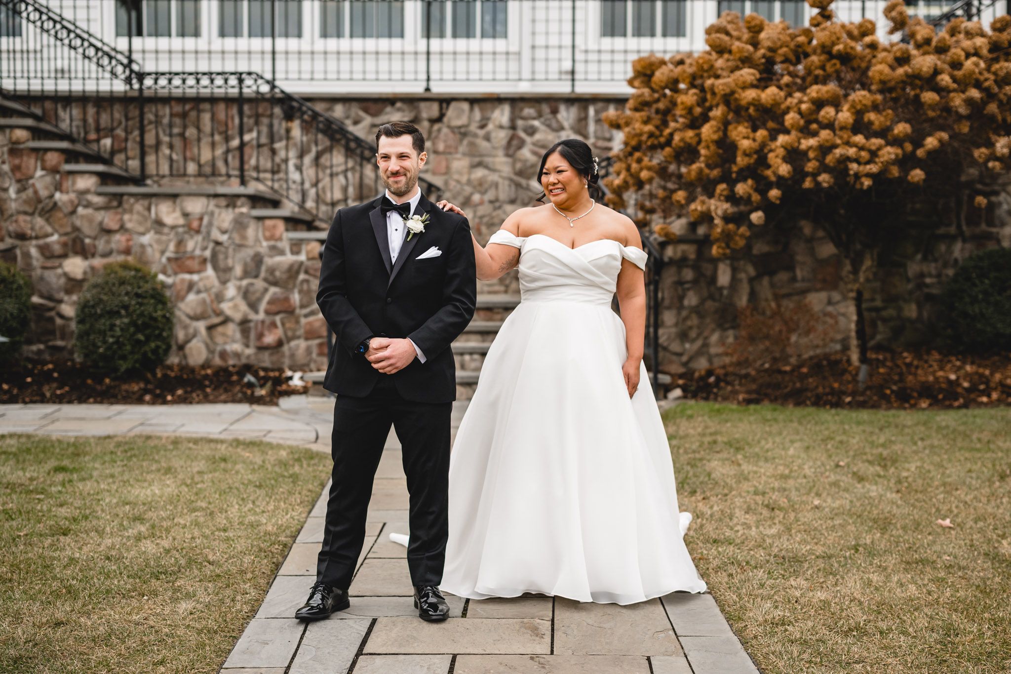 A bride and groom stand together on a stone walkway surrounded by fall colors and architecture.