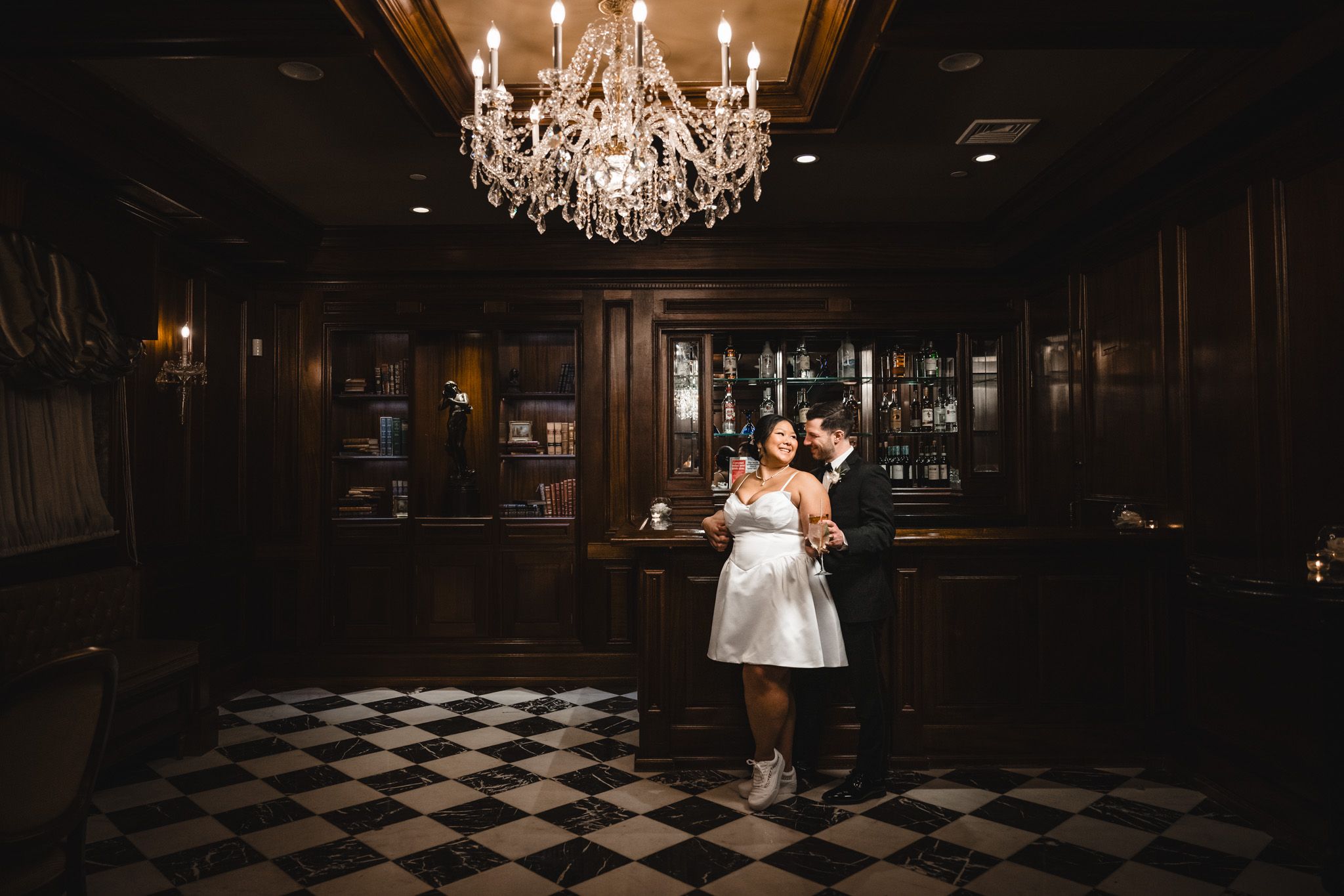 Dark and moody wedding venue interior with dramatic chandelier lighting and checkered floor.