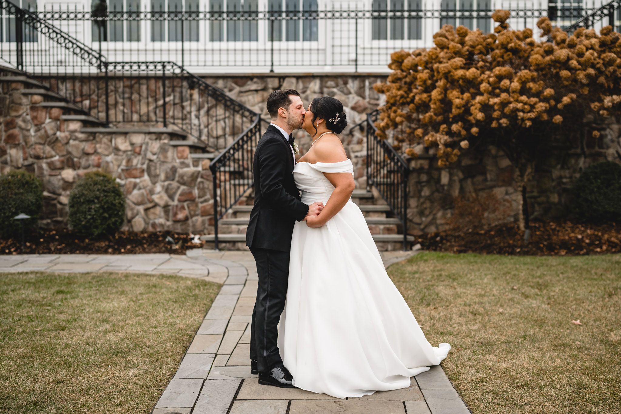 A romantic wedding moment captured on a stone path with rustic stone walls and autumn foliage.